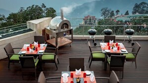 A rooftop restaurant with outdoor seating, a pizza oven, and a scenic mountain view. - Mosaic Mussoorie (Dehradun)