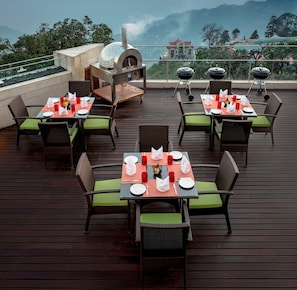 A rooftop restaurant with outdoor seating, a pizza oven, and a scenic mountain view.