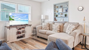 Een woonkamer met een televisie, een bank, een salontafel en een boekenplank.