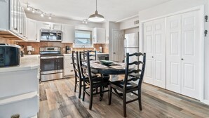 Een moderne keuken met witte kasten, roestvrijstalen apparatuur, een eettafel met stoelen en een hanglamp.