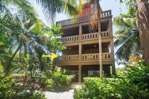 Un edificio de varios pisos con balcones, rodeado de exuberante vegetación tropical.