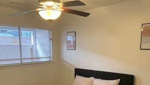 Un dormitorio con cama, ventilador de techo, ventana con persianas, mesita de noche y alfombra.