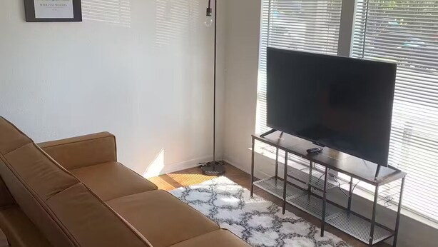 Una sala de estar con un sofá marrón, un televisor sobre un mueble bajo y un cuadro en la pared.