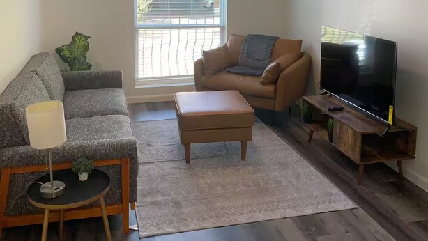 Ein Wohnzimmer mit einer Couch, einem Couchtisch, einem Fernseher auf einem Holzständer, einem Deckenventilator und einem Fenster mit Jalousien.