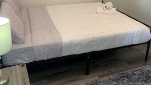 Ein Einzelbett mit weißer Matratze und Kissen, eine Nachttischlampe und ein gerahmtes Bild an der Wand.