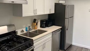 Eine moderne Küche mit weißen Schränken, einem Edelstahlkühlschrank, einem schwarzen Herd und einer Kaffeemaschine.
