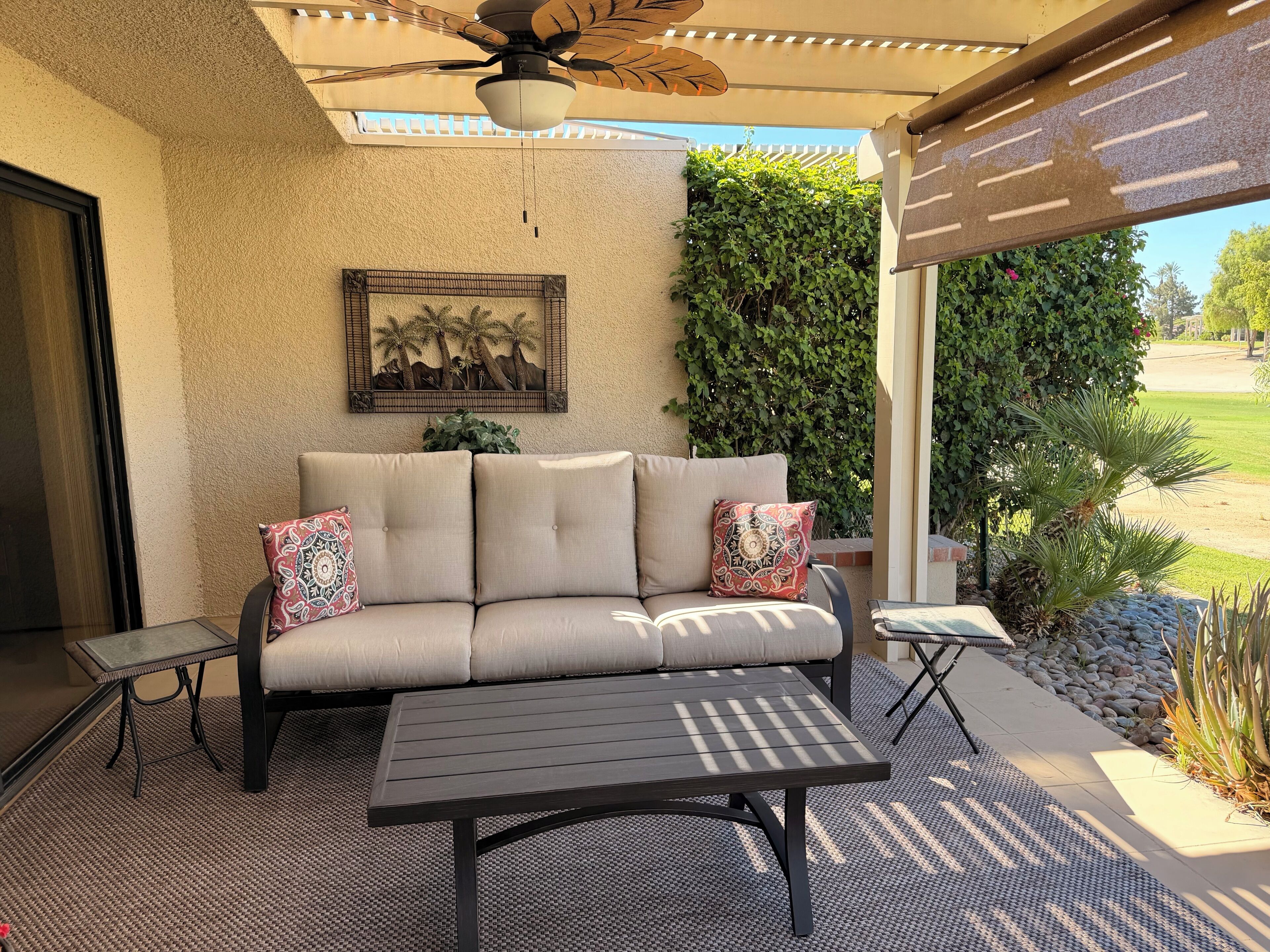 A covered patio area with a sofa, a table, and a ceiling fan.