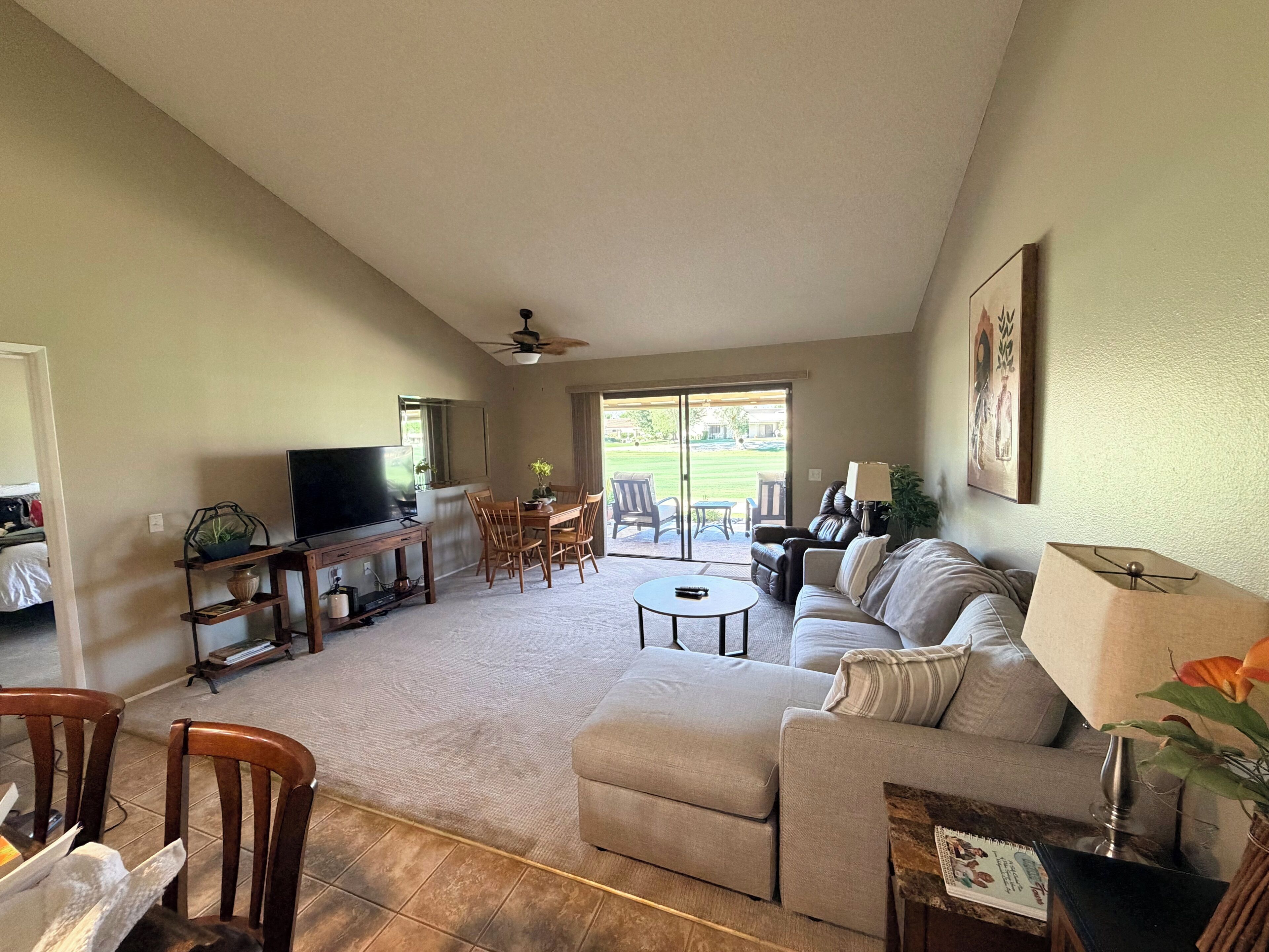 A living room with a TV, sofa, chairs, a dining table, and a ceiling fan.