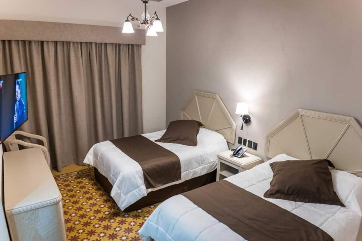 A hotel room with two beds, a TV, a desk, and a chandelier.