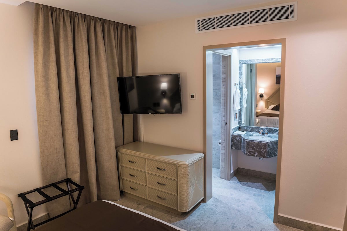 A hotel room with a TV, a bedside table, a dresser, and a bathroom visible through an open door.