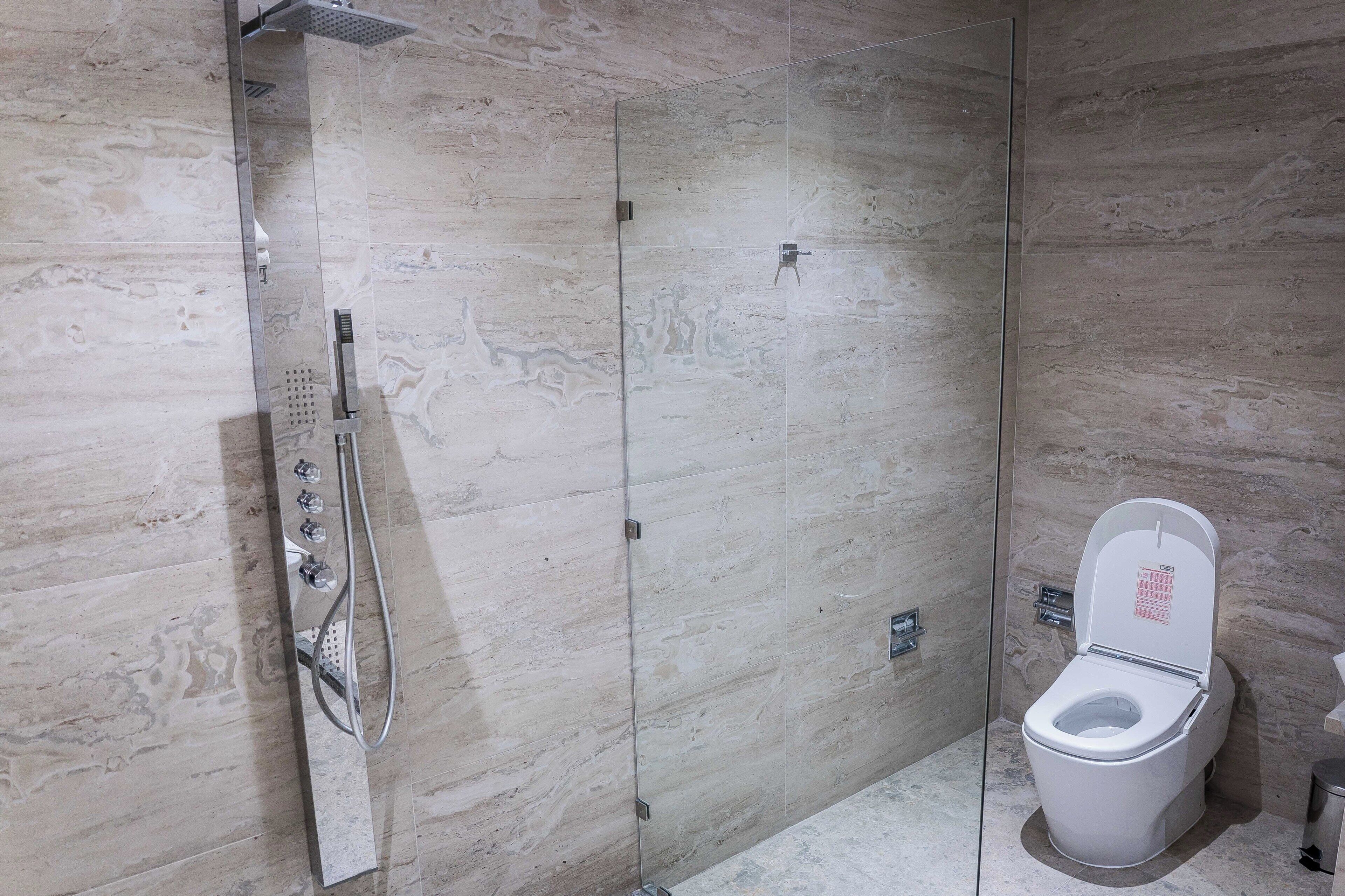 A bathroom with a shower, toilet, and marble walls.