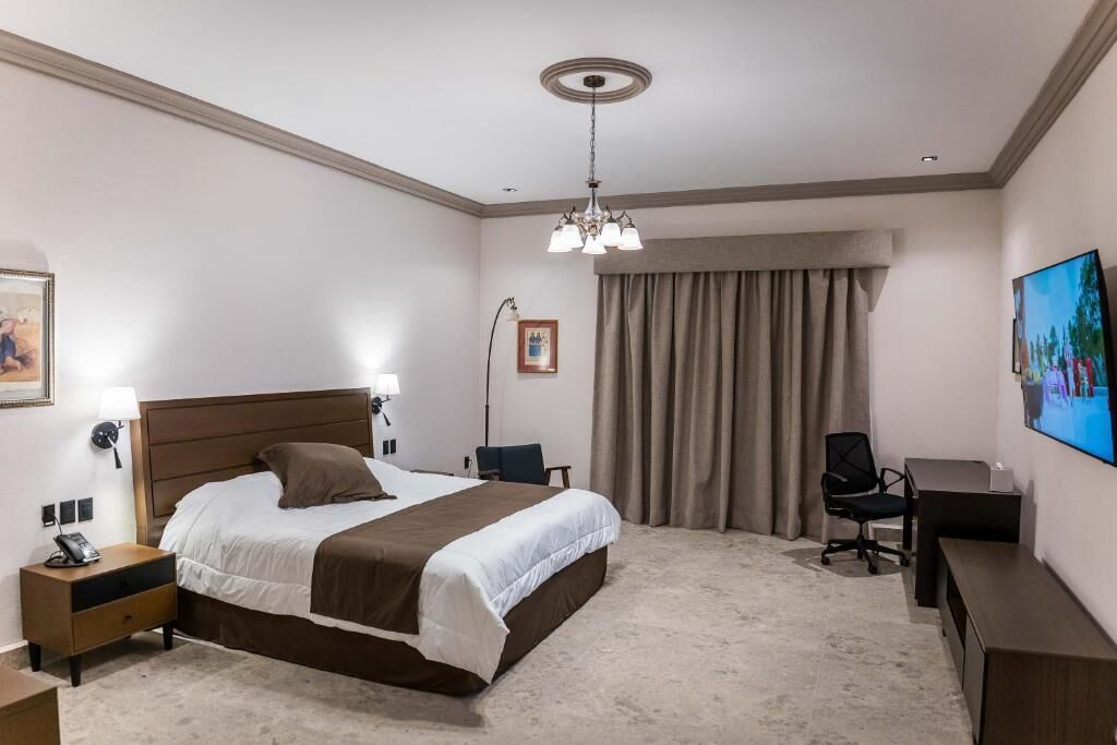 Una habitación de hotel con cama, escritorio, silla y televisión en la pared.