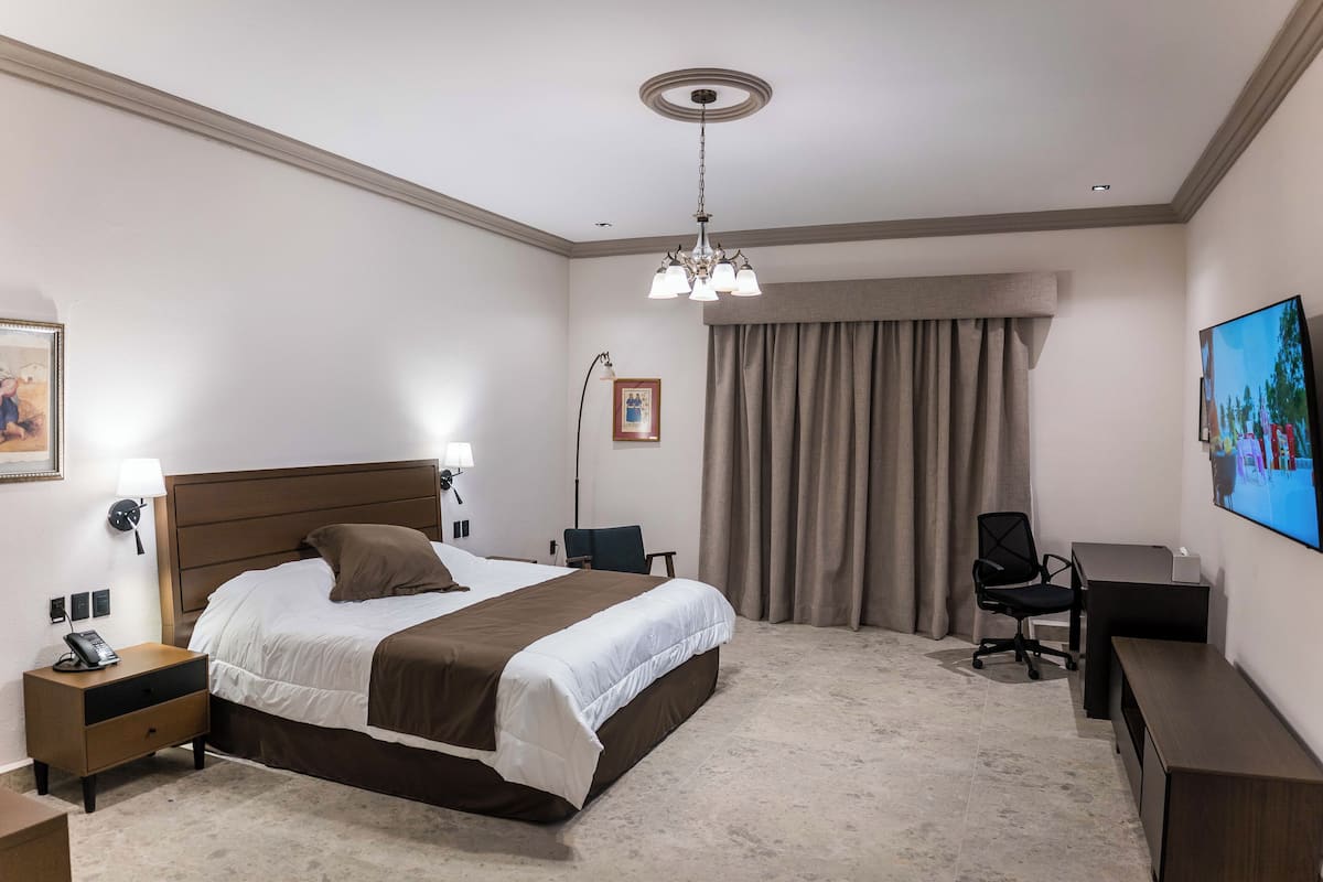 A hotel room with a bed, desk, chair, and a television on the wall.