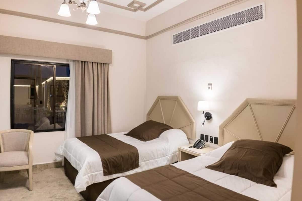 A hotel room with two beds, a chair, a nightstand with a phone, and a window with curtains.