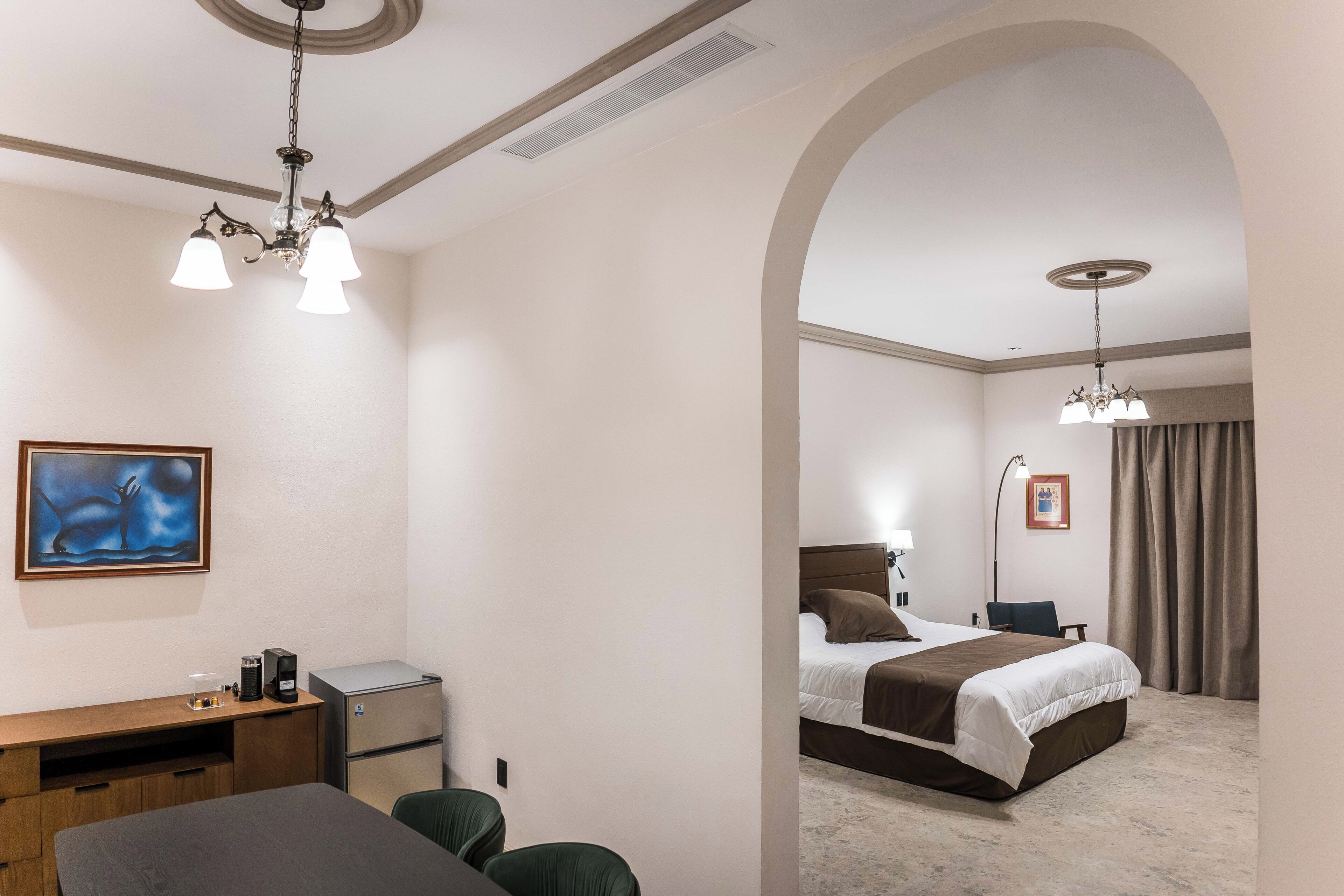 A hotel room with a desk, chair, bed, and artwork.