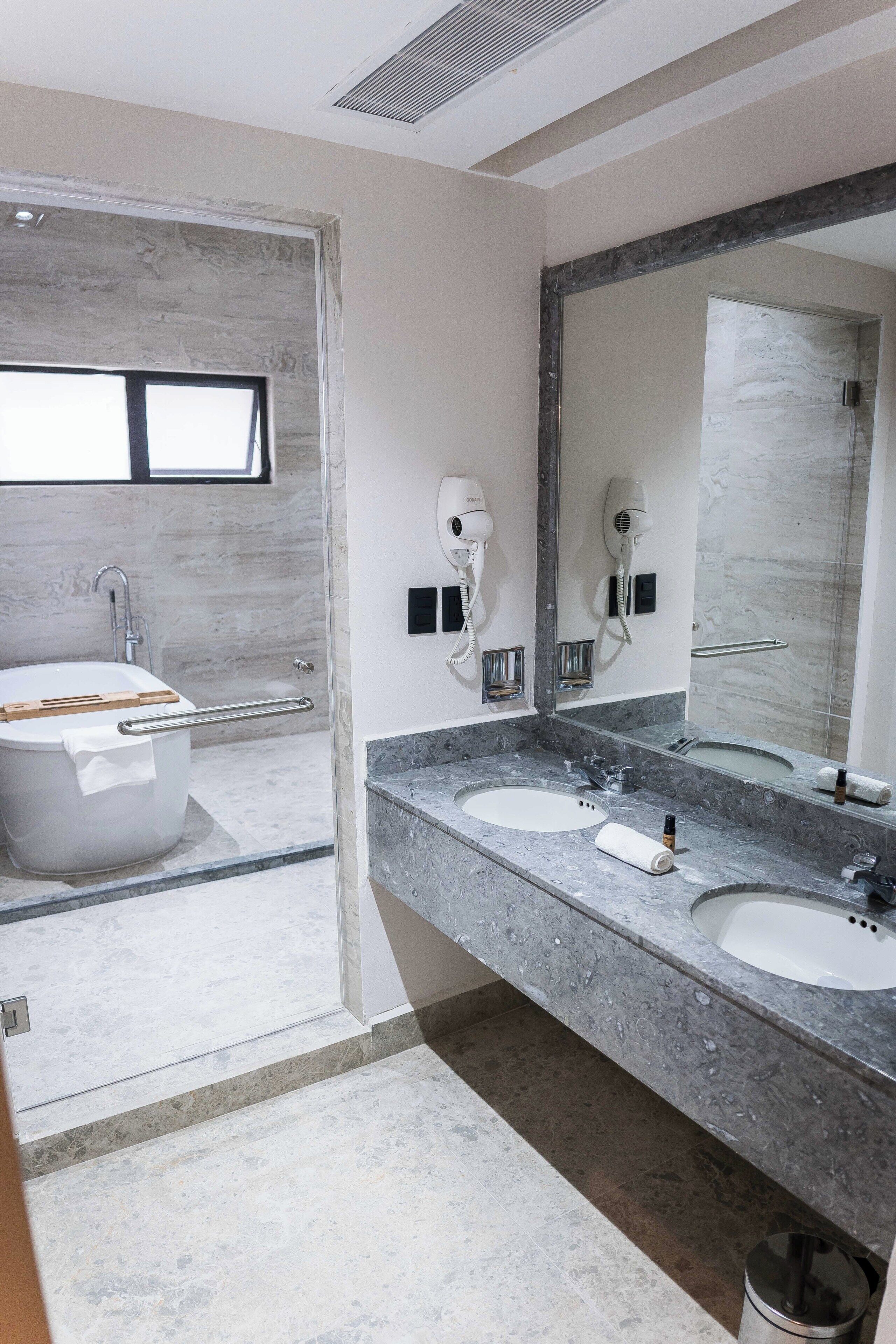 A modern bathroom with a bathtub, two sinks, and a large mirror.