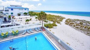 Une piscine surveillée par un maître-nageur, une plage et un bâtiment avec un toit bleu.