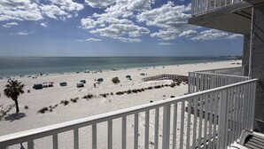 Une vue sur la plage depuis un balcon doté d’une balustrade, avec un ciel dégagé et une mer calme.