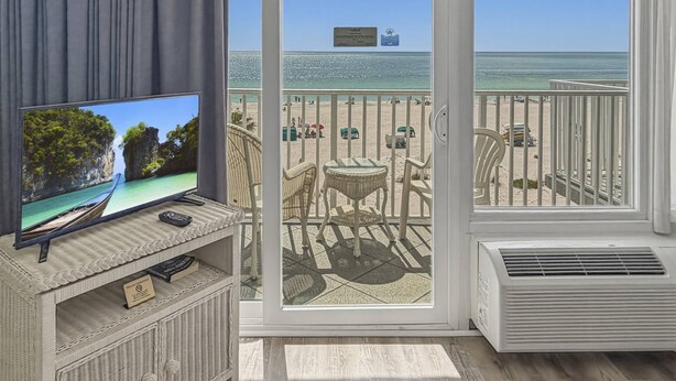 Un balcon équipé d’un téléviseur, de meubles en osier et offrant une vue sur la plage.
