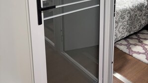 Ein Zimmer mit einer Schiebetür aus Glas, einem Bett mit gemusterten Bettbezügen, einem roten Kopfkissen und einem Teppich mit Muster.