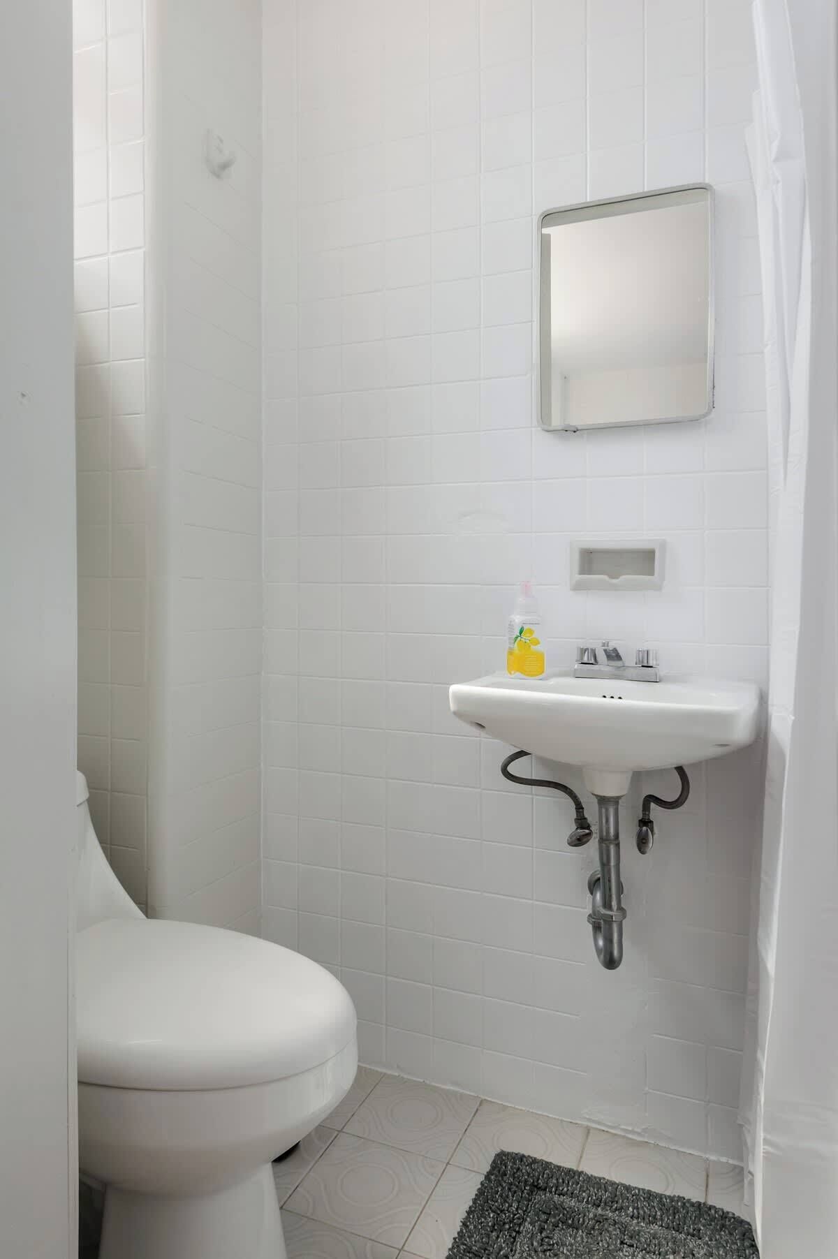 Un baño pequeño y blanco con inodoro, lavamanos y espejo.