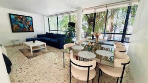 A modern living room with a blue sofa, a white coffee table, and a glass dining table with chairs. - 4BR apartment | Private Balcony · Near Masaryk (Mexico City)