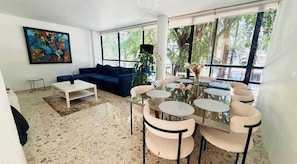 A modern living room with a blue sofa, a white coffee table, and a glass dining table with chairs. - 4BR apartment | Private Balcony · Near Masaryk (Mexico City)