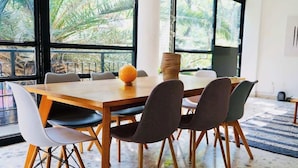 A dining area with a wooden table, six chairs, and a large window with a view of palm trees. - Boutique Apt | Polanco - Masaryk (Mexico City)