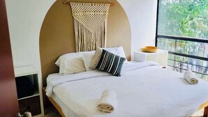A bedroom with a bed, pillows, a macrame wall hanging, a bedside table, and a window with a view. - Boutique Apt | Polanco - Masaryk (Mexico City)