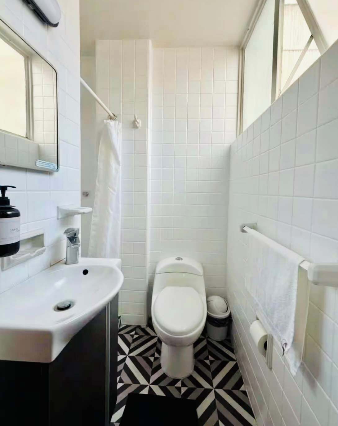 Un baño pequeño con azulejos blancos, un inodoro, un lavamanos y una cortina de ducha.