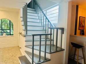 Eine Treppe mit Metallgeländern, ein Fenster mit Blick auf Grünflächen und ein Barhocker.
