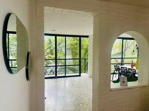 Ein Innenraum mit großem Fenster, einem Spiegel und Blick auf einen Außenbereich mit Stühlen und Tischen.