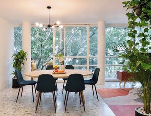 A dining area with a round table, chairs, a ceiling light fixture, and large windows with a view of trees. - Two-Level PH | Polanco · Near Masaryk · 4BR (Mexico City)