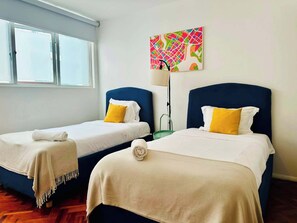 A hotel room with two beds, each with a blue headboard and white bedding. There is a colorful abstract painting on the wall above the beds. - Two-Level PH | Polanco · Near Masaryk · 4BR (Mexico City)