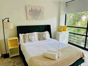 A hotel room with a bed, a bedside table, a lamp, a window with a view of greenery, and a cityscape artwork on the wall. - Two-Level PH | Polanco · Near Masaryk · 4BR (Mexico City)