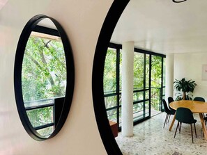 A modern interior with a round table and chairs, large windows, and a view of greenery outside. - Two-Level PH | Polanco · Near Masaryk · 4BR (Mexico City)