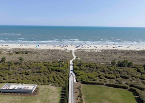 Een kuststrand met een pad dat leidt naar een gebouw met een plat dak en een zwembad.