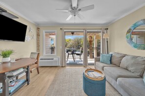 A living room with a flat-screen TV, a ceiling fan, a sofa, a coffee table, and a dining area with a table and chairs. - Beachside Bliss - Beachfront Condo! (Hilton Head Island)