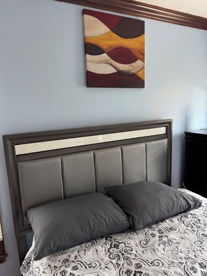 Ein Bett mit Kopfstütze, zwei Kissen und einer gemusterten Tagesdecke.