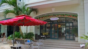 An outdoor seating area with a red umbrella, white chairs, and a palm tree. - Elene Hotel (Phu Quoc)