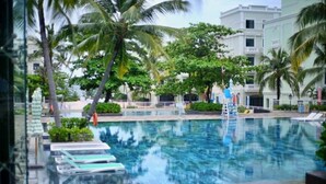 A swimming pool with lounge chairs, palm trees, and a building in the background. - Elene Hotel (Phu Quoc)
