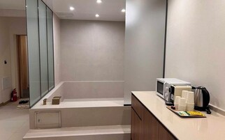 Un baño moderno con cabina de ducha de vidrio, tocador con microondas, tazas de café y tetera.