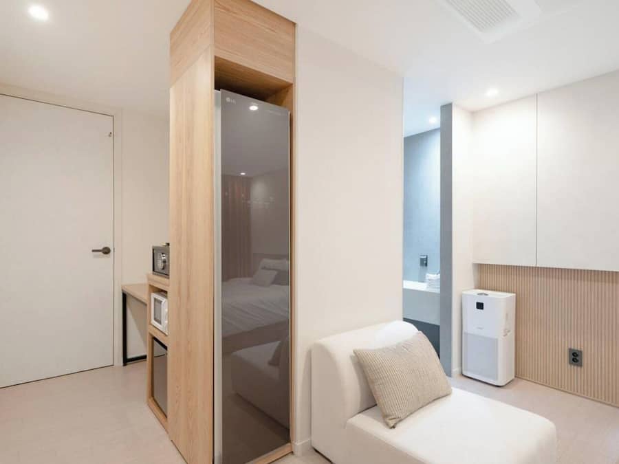 Una habitación de hotel moderna con una cama, una zona de estar, un escritorio pequeño con microondas y aire acondicionado de pared.