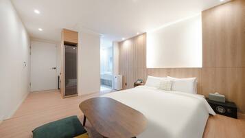 Quarto de hotel moderno com uma cama grande, escrivaninha de madeira, um espaço de estar pequeno e um closet espaçoso.