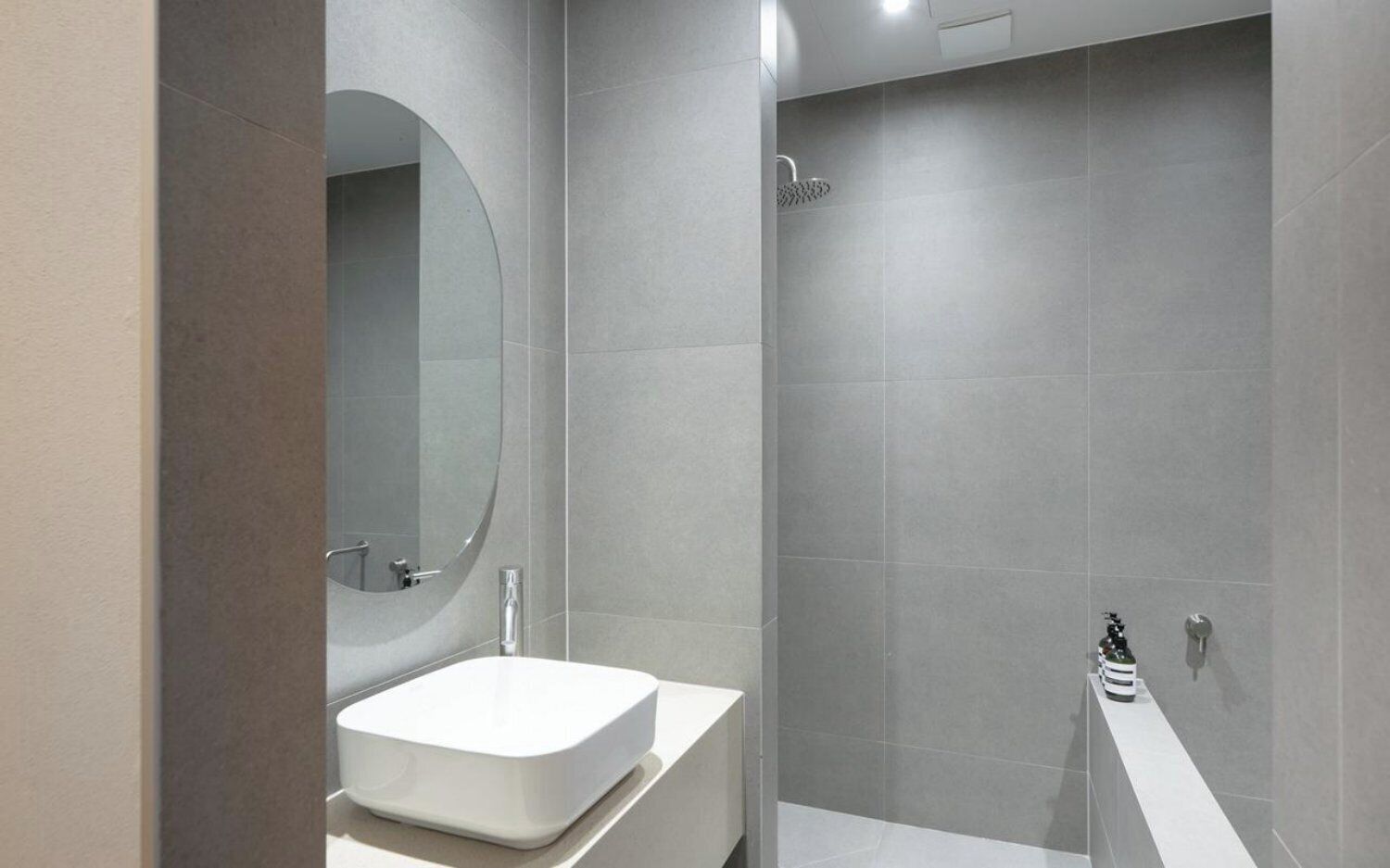 A modern bathroom with a white sink, a large mirror, and a shower area.
