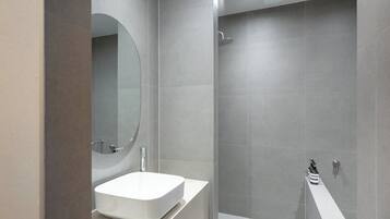 Un baño moderno con un lavamanos blanco, un espejo grande y una zona de ducha.
