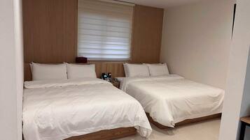Ein Hotelzimmer mit zwei Betten, einem Holzkopfende, einem Nachttisch mit Telefon und einem Fenster mit Jalousien.