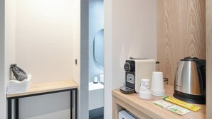Una camera d'albergo con un tavolo in legno, una macchina del caffè, un bollitore e una piccola pila di tazze bianche.