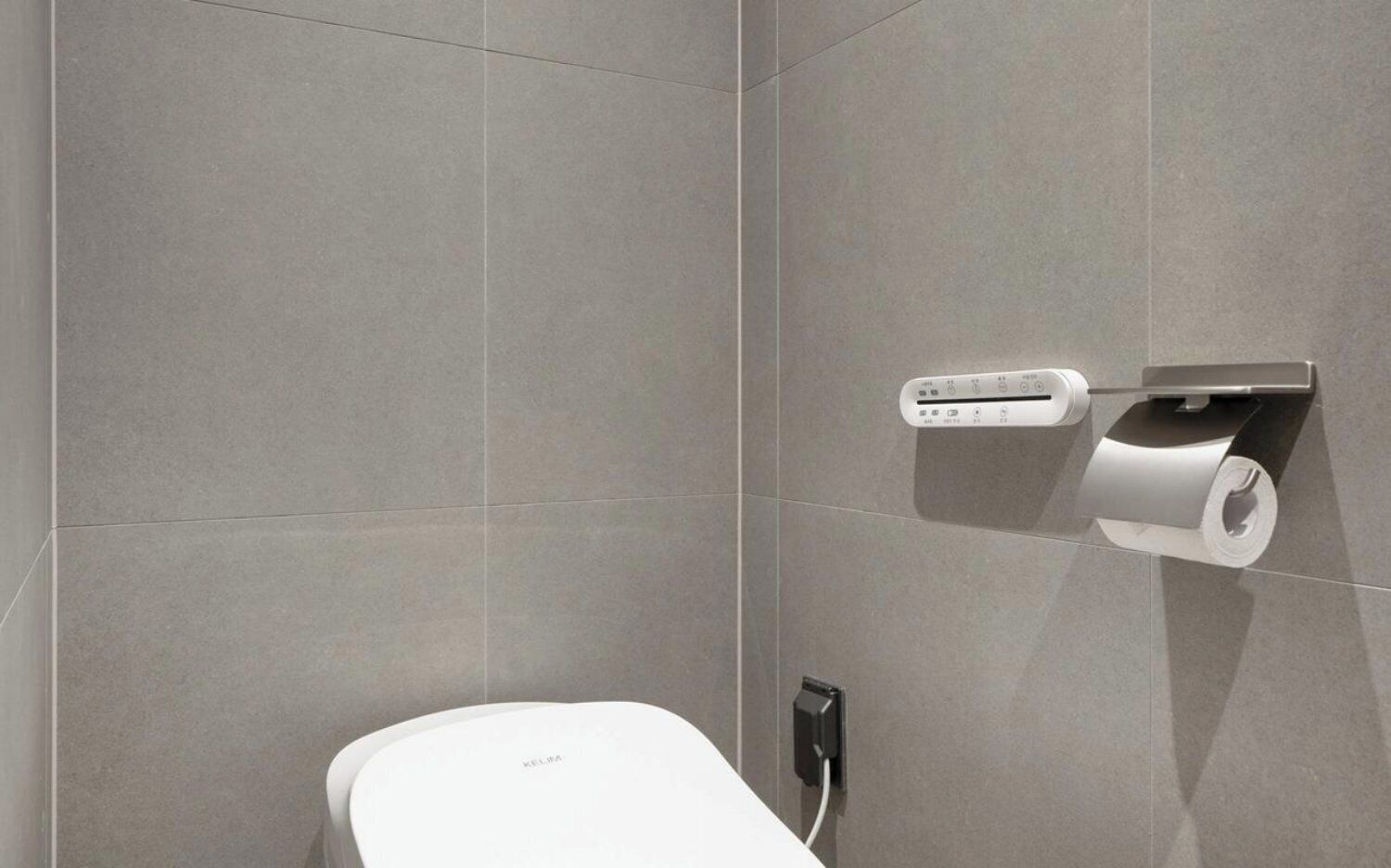 A modern bathroom with a toilet, a wall-mounted paper dispenser, and a power outlet.