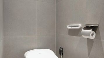 A modern bathroom with a toilet, a wall-mounted paper dispenser, and a power outlet.